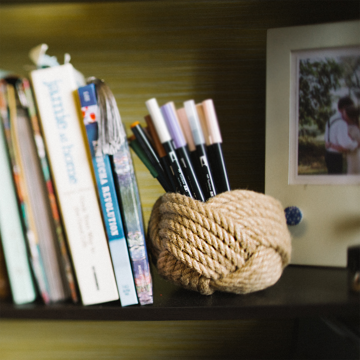 Books and framed photo on a shelf with pens in a rope holder, home office decor.