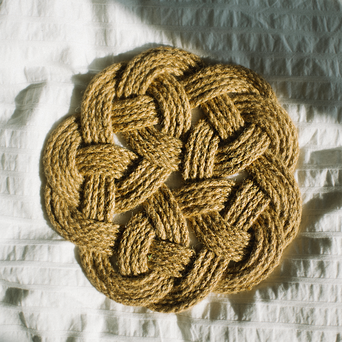 Woven natural fiber rope mat with an intricate knot design on a white textured surface