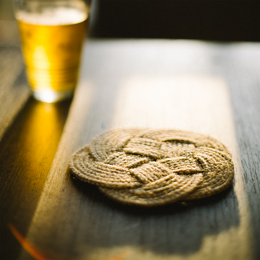 Woven coaster on a wooden table with a glass of yellow drink in the background
