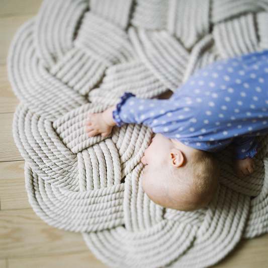 Baby in blue polka dot outfit on braided rope mat, safe play area, portable kids product