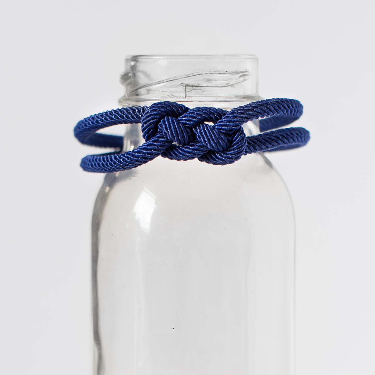Navy blue knotted rope bracelet displayed on clear glass bottle, travel safety accessory