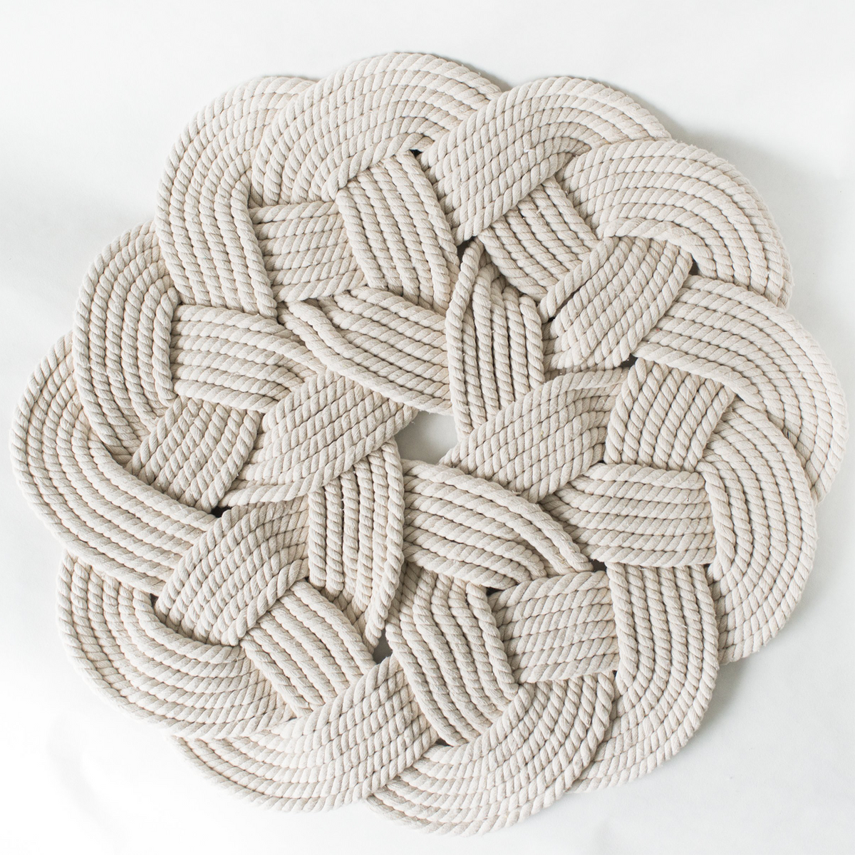 Round white braided rope mat with intricate knot design, photographed on a plain background.