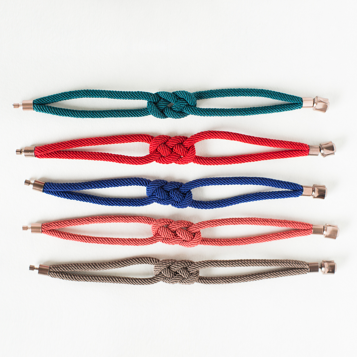 Five colorful knotted rope bracelets with metal ends, arranged on a white background.