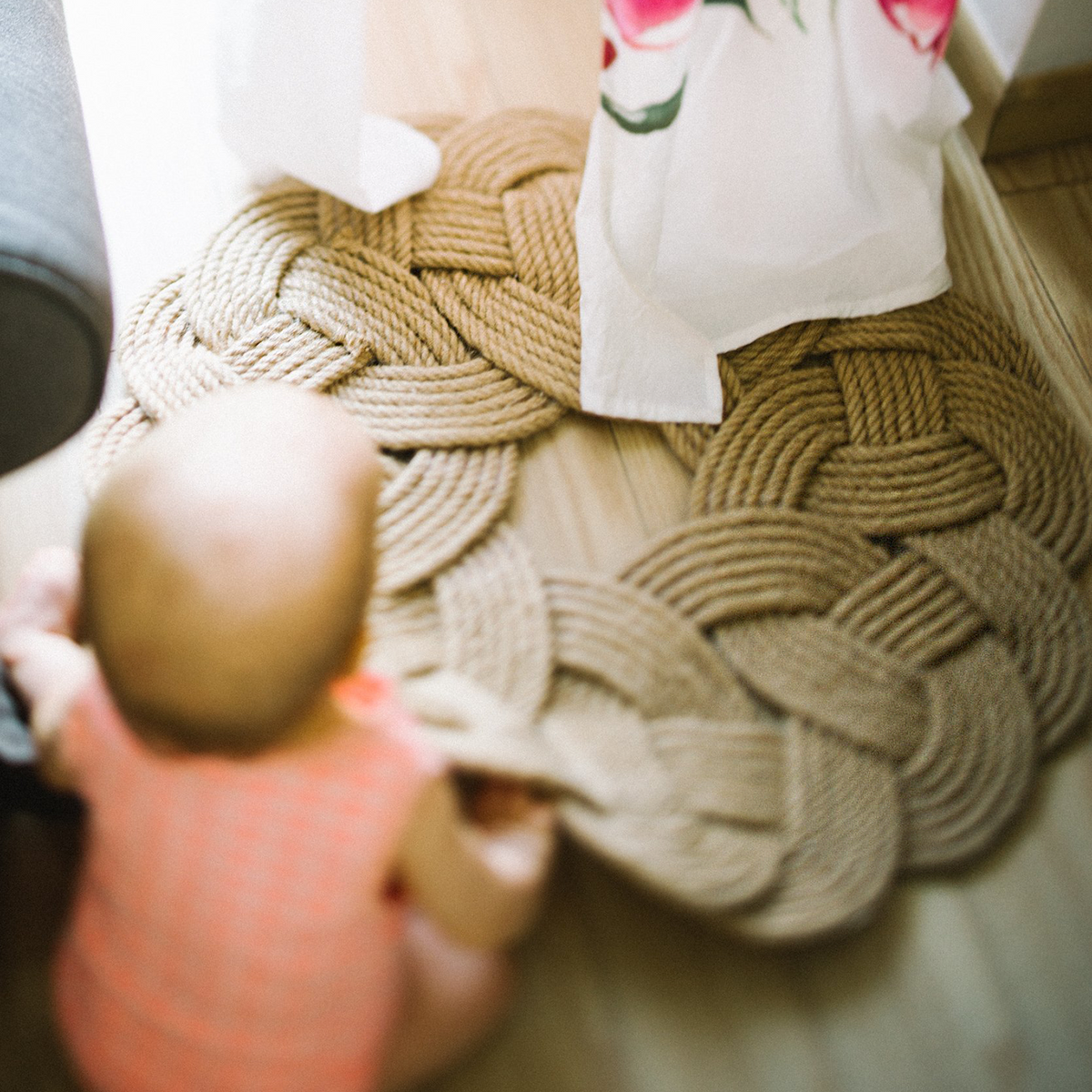 Baby sitting near braided rope mat on wooden floor, natural light, safe home decor