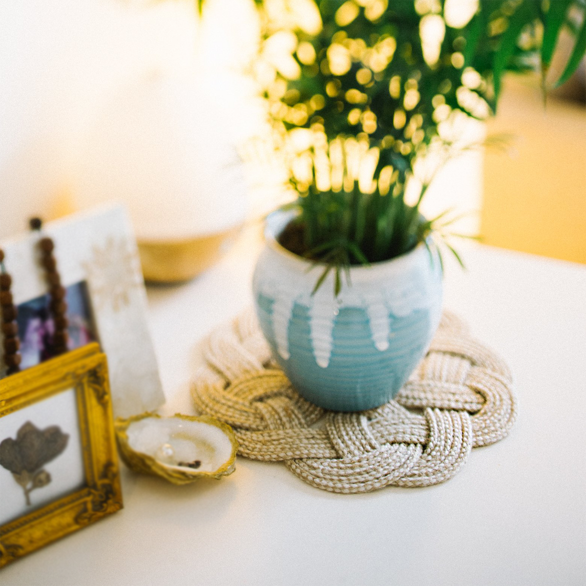 Blue ceramic plant pot on woven mat, framed photos, and décor on white table